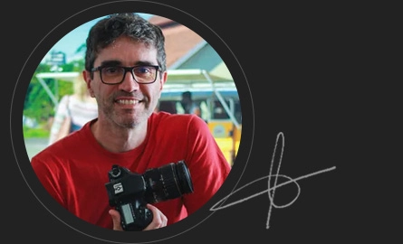 Le Daros sorrindo com uma c�mera na m�o e ao lado direito sua assinatura.